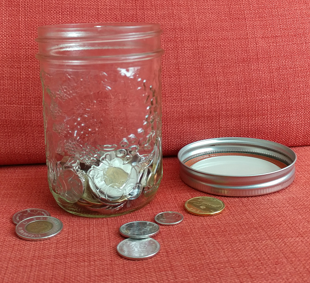 A jam jar with Canadian coins inside, lid is to the right of the jar