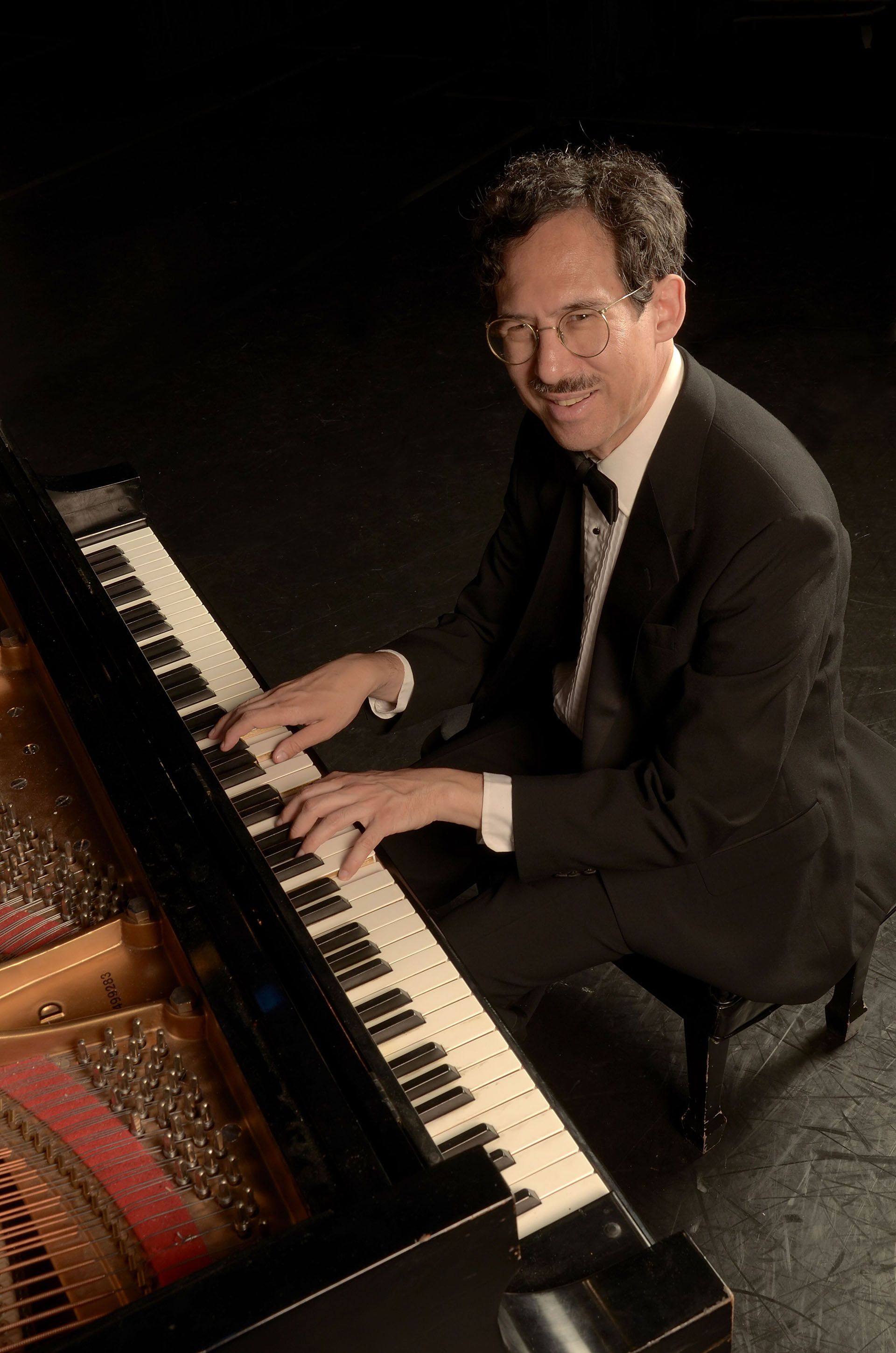 Michael Arnowitt wearing a tux and smiling while playing grand piano.